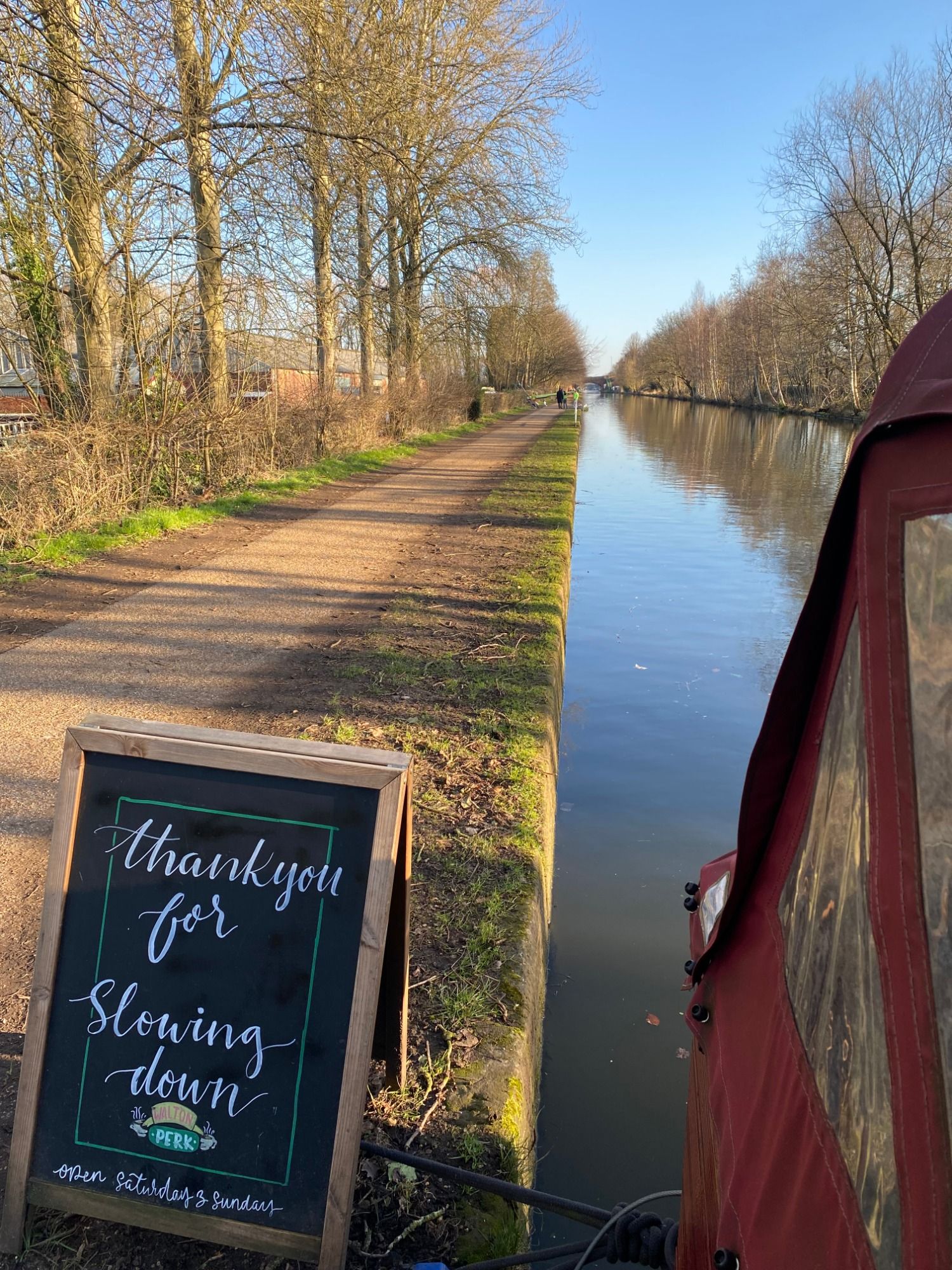 The Bridgewater Canal towpath beside Walton Perk, with the boat's canopy and a chalkboard sign in view